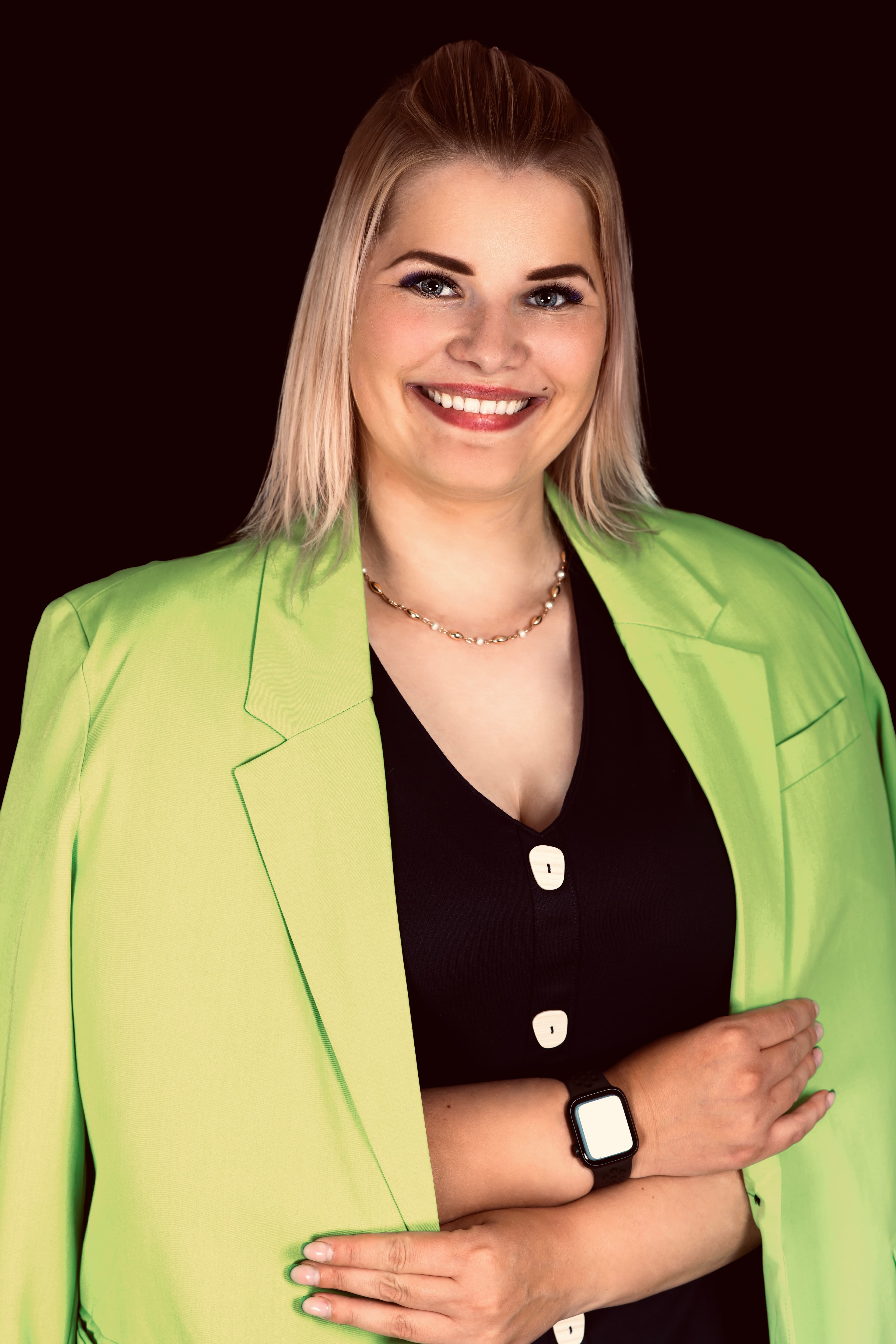 Smiling blonde woman wearing a lime green blazer and black top against a black background.
